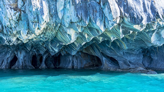 Turquoise water in front of a beautiful, intricately carved marble cave formation.