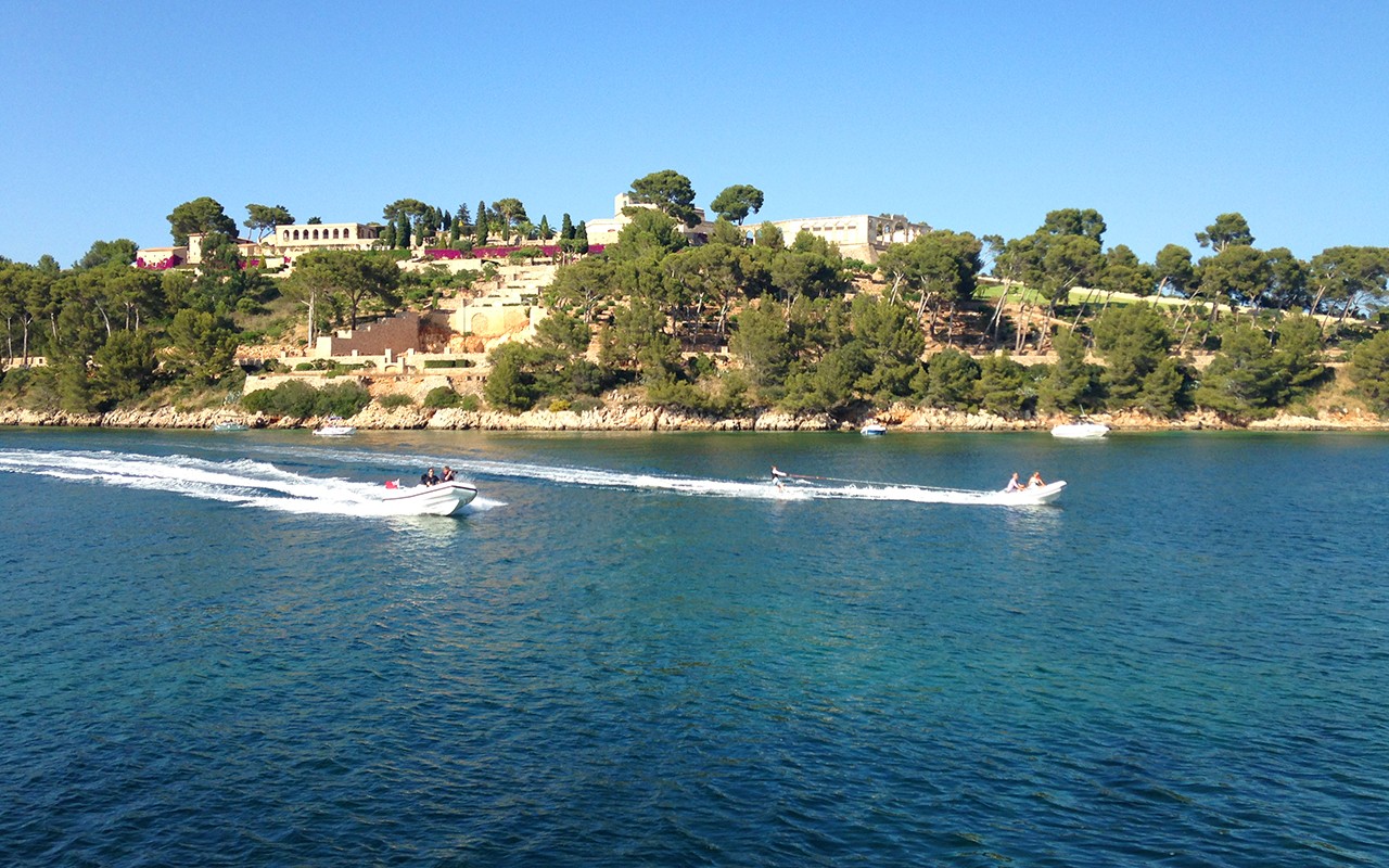 A speedboat pulling a waterskier near a lush island with clear, blue skies.