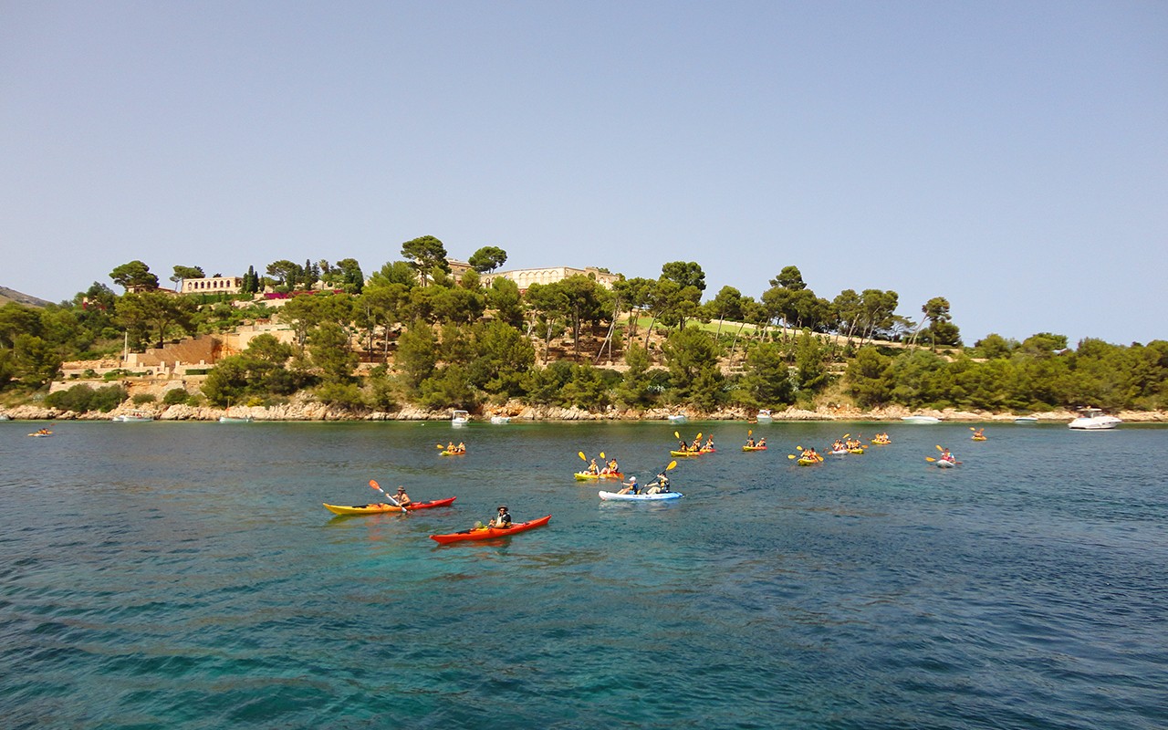 A scenic view of kayakers enjoying the water near a lush, green island under clear skies.