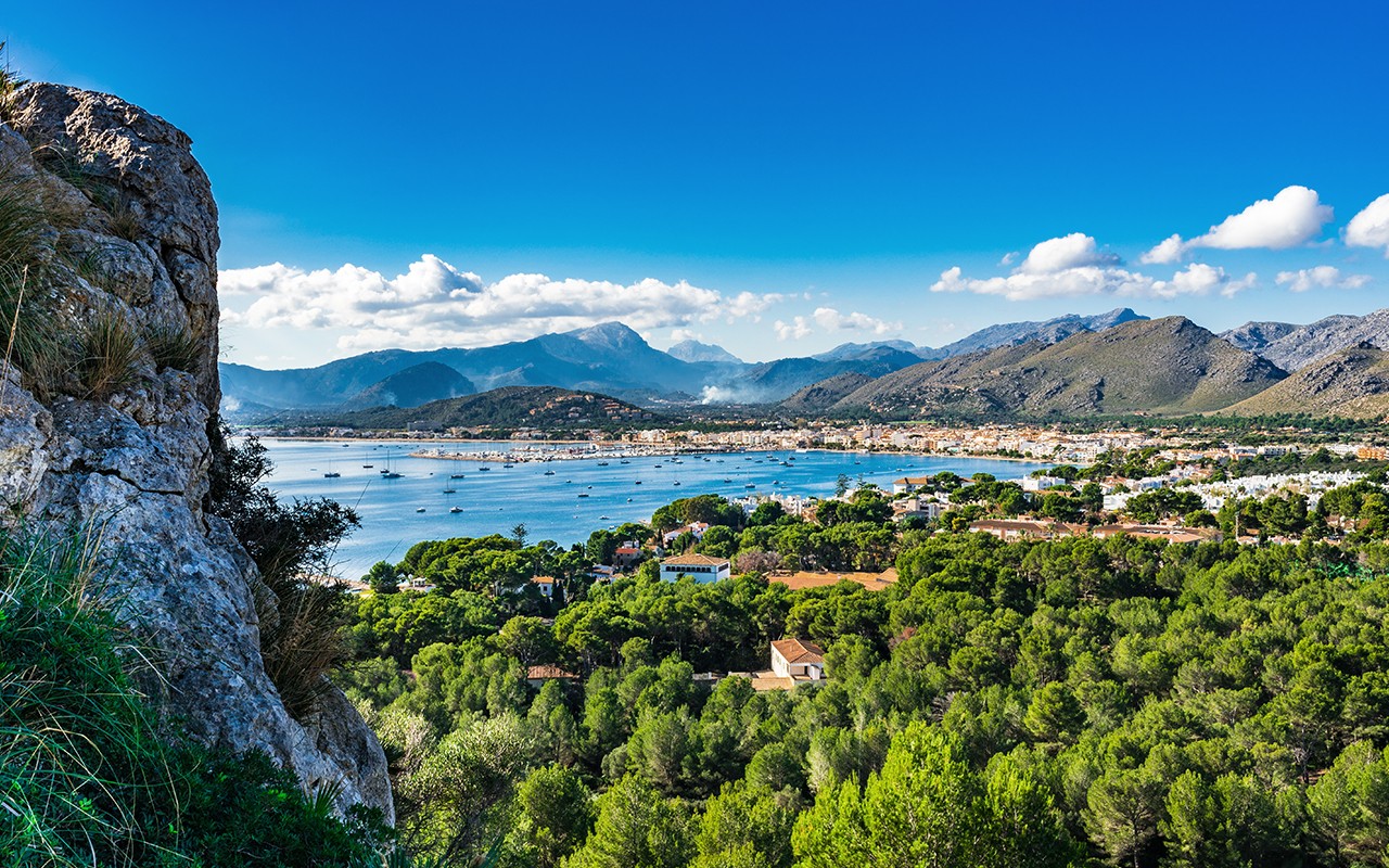 A picturesque bay surrounded by lush greenery and mountains, with boats scattered across the water.