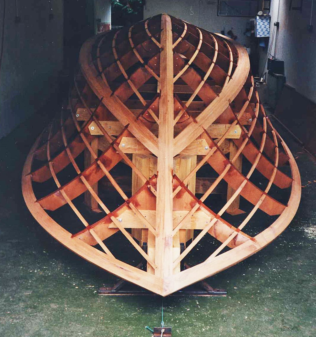 A wooden boat frame under construction, showing intricate ribbing and structural support.