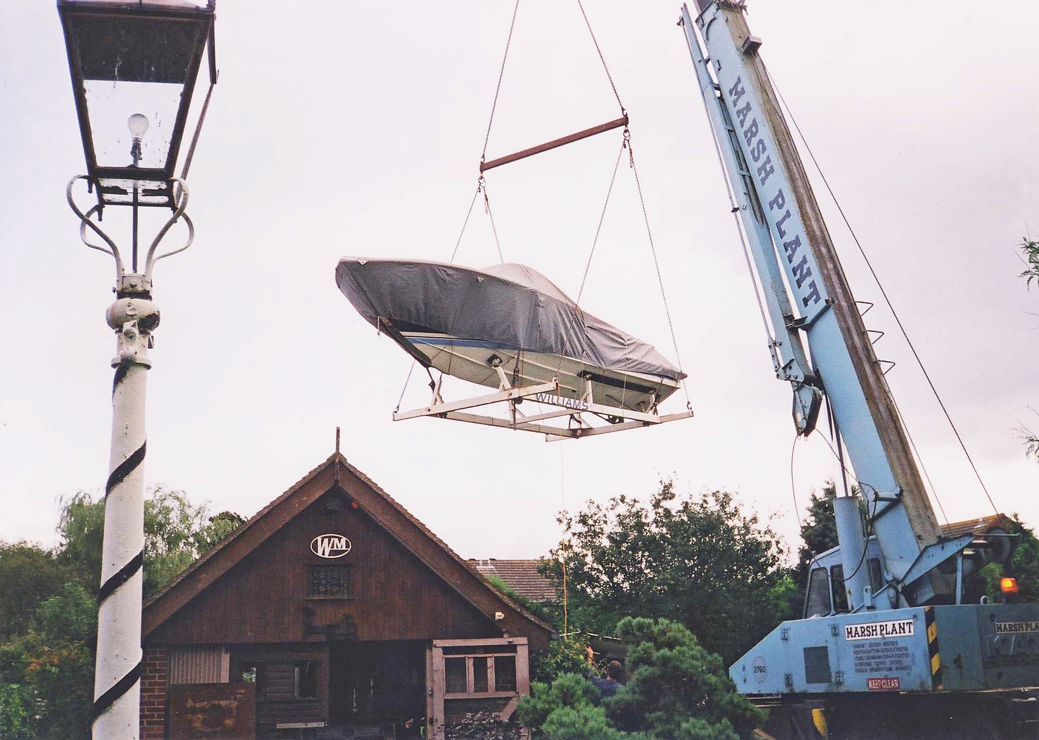 A crane lifting a covered boat outside a Williams building with a Marsh Plant crane.
