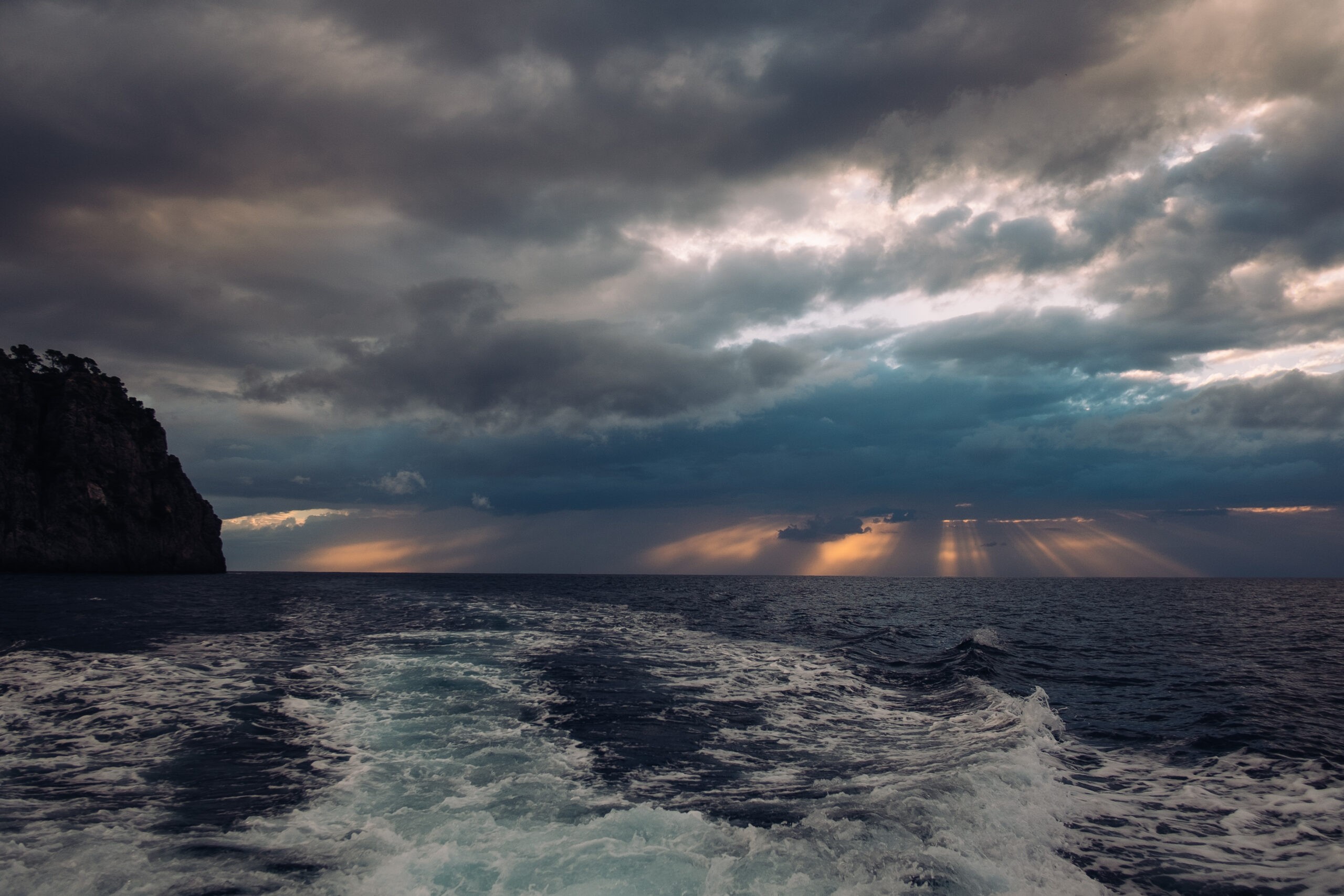 A dramatic seascape with stormy clouds, sun rays, and a view from a boat's wake.