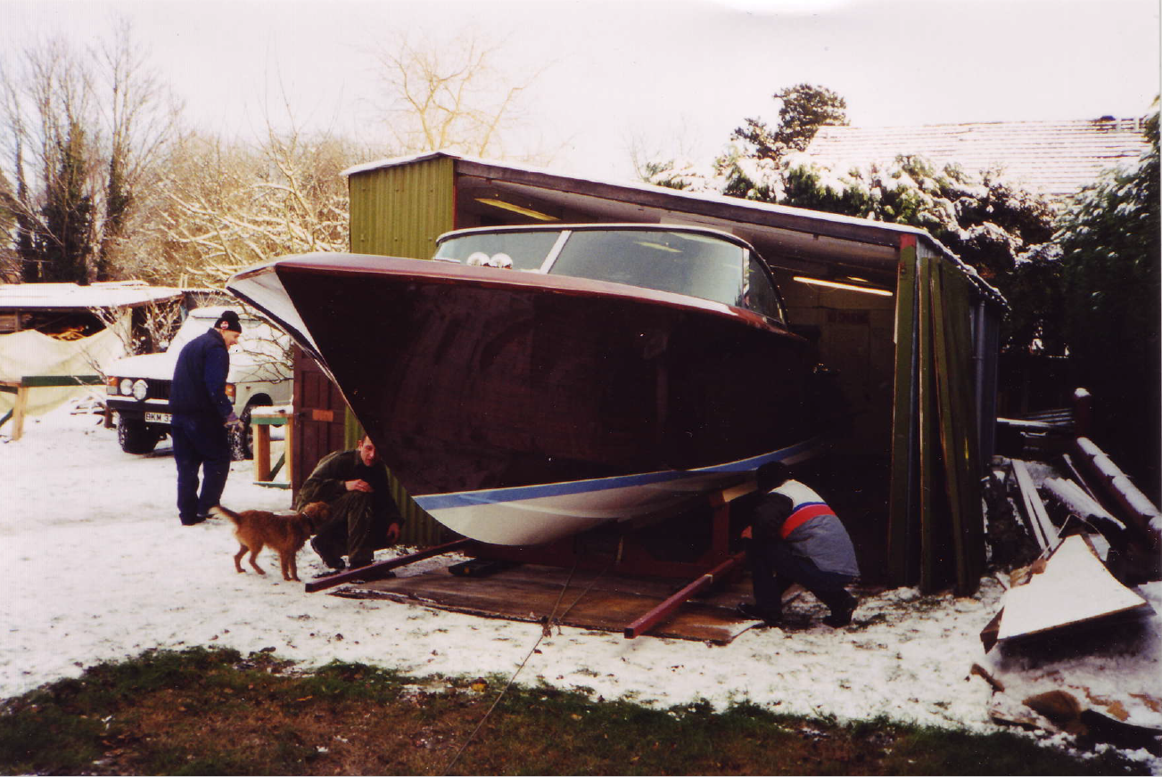 A boat in a shed being worked on by three men, with snow on the ground.