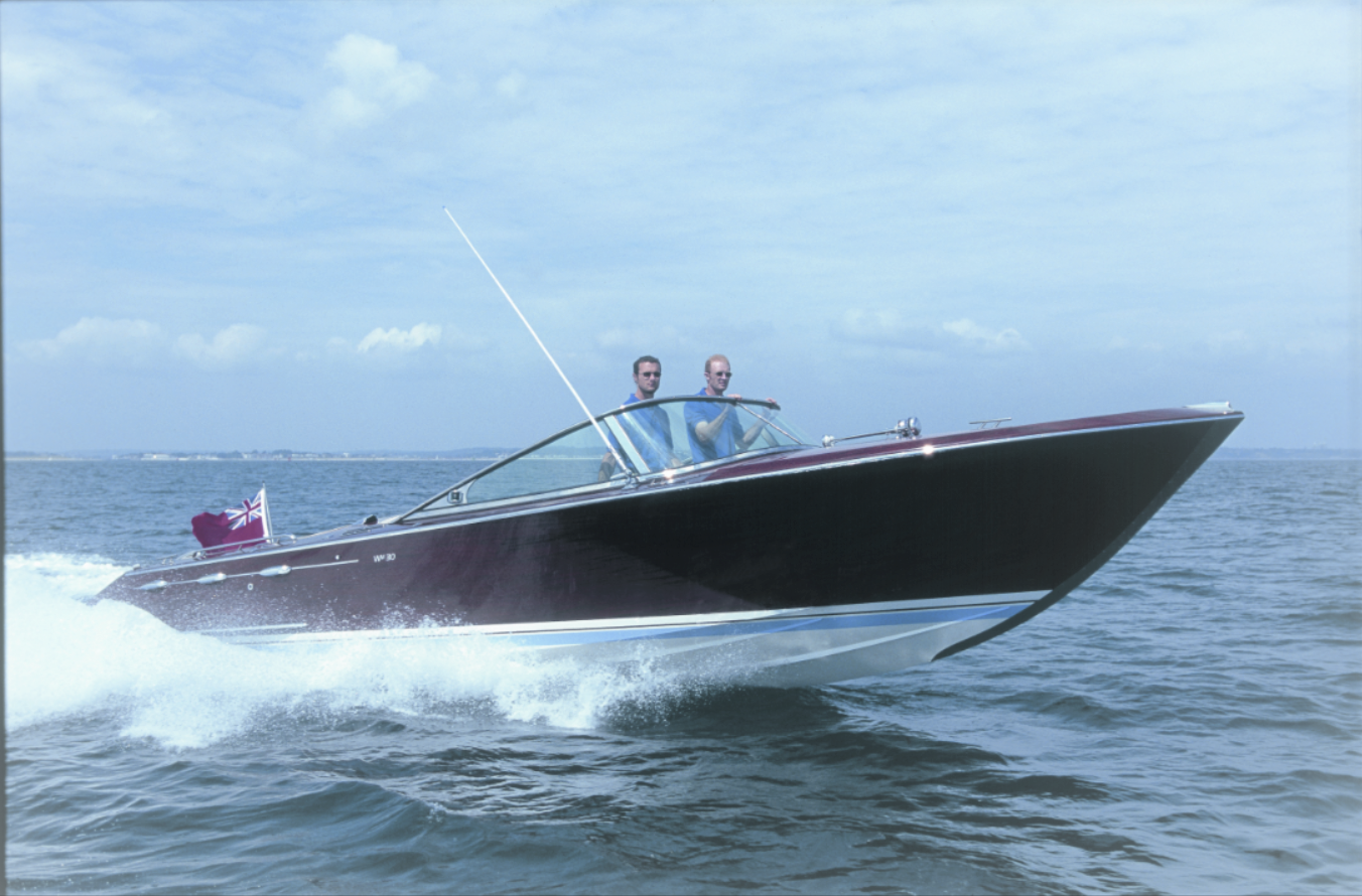 A sleek, dark-colored speedboat gliding on the water with two men on board.