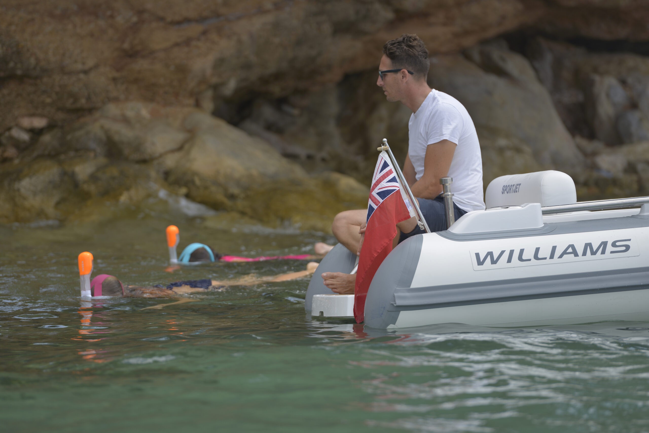 Two people snorkeling close to a yacht tender with an onlooker onboard.
