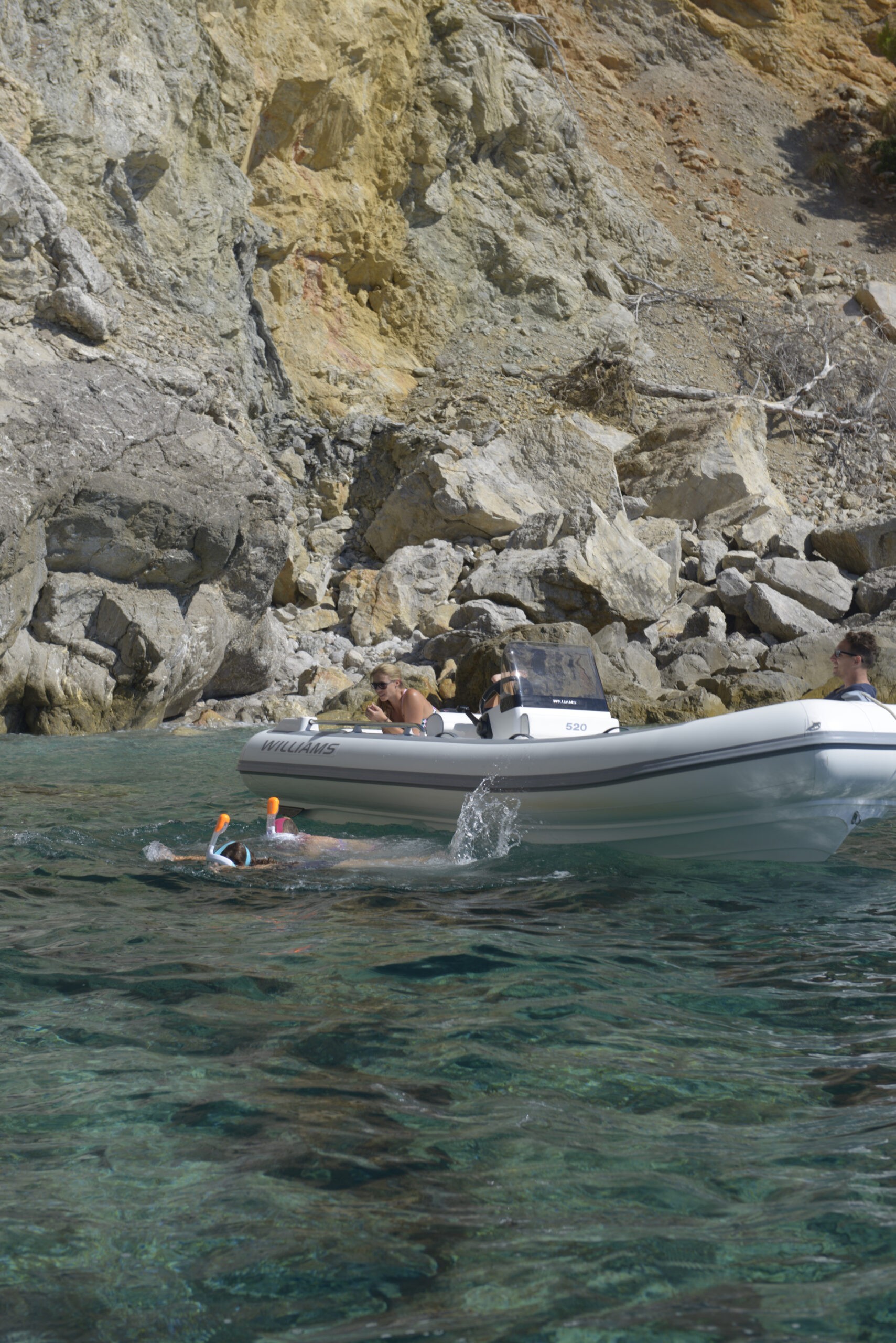 Lightweight tender anchored in a secluded cove, with snorkelers diving into the serene blue depths just beside it.