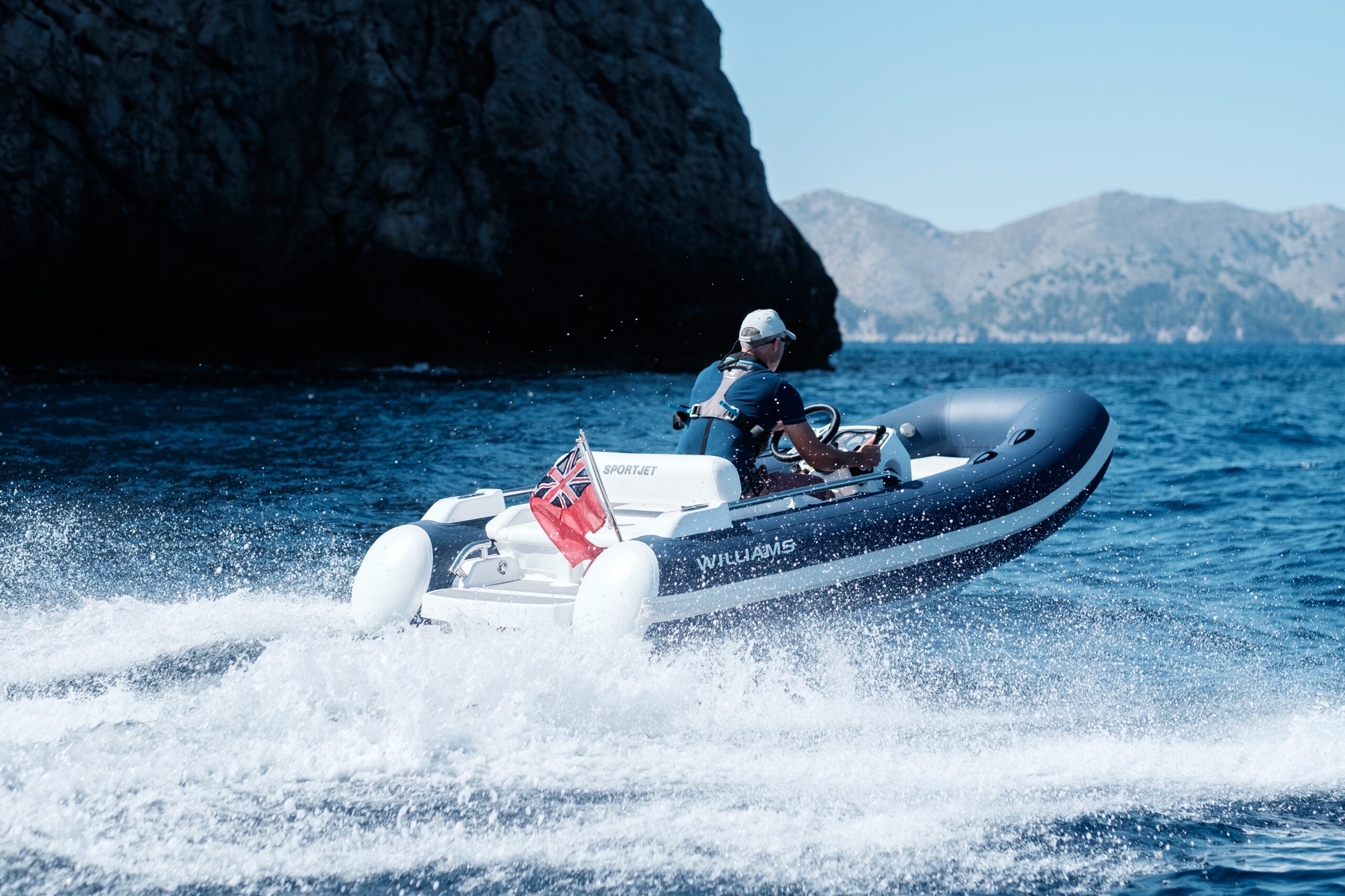 A man driving a Williams SportJet Tender near rocky cliffs.