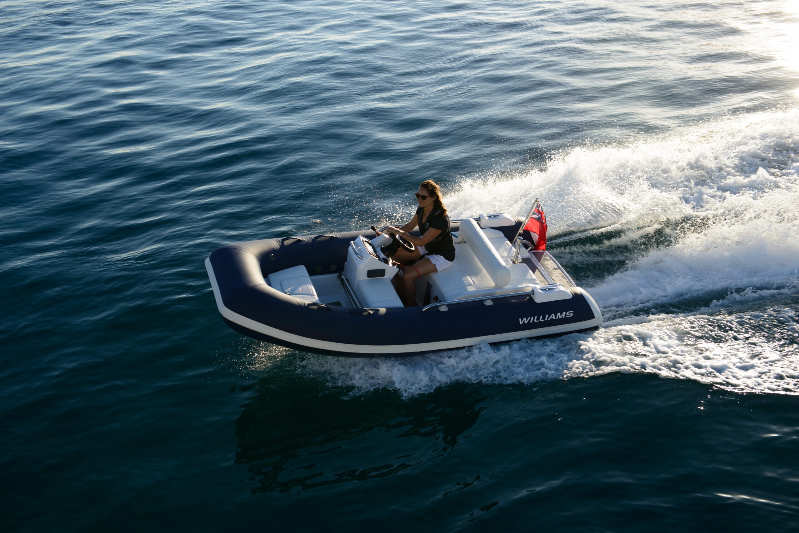 A woman steering a small tender boat by Williams on calm waters.