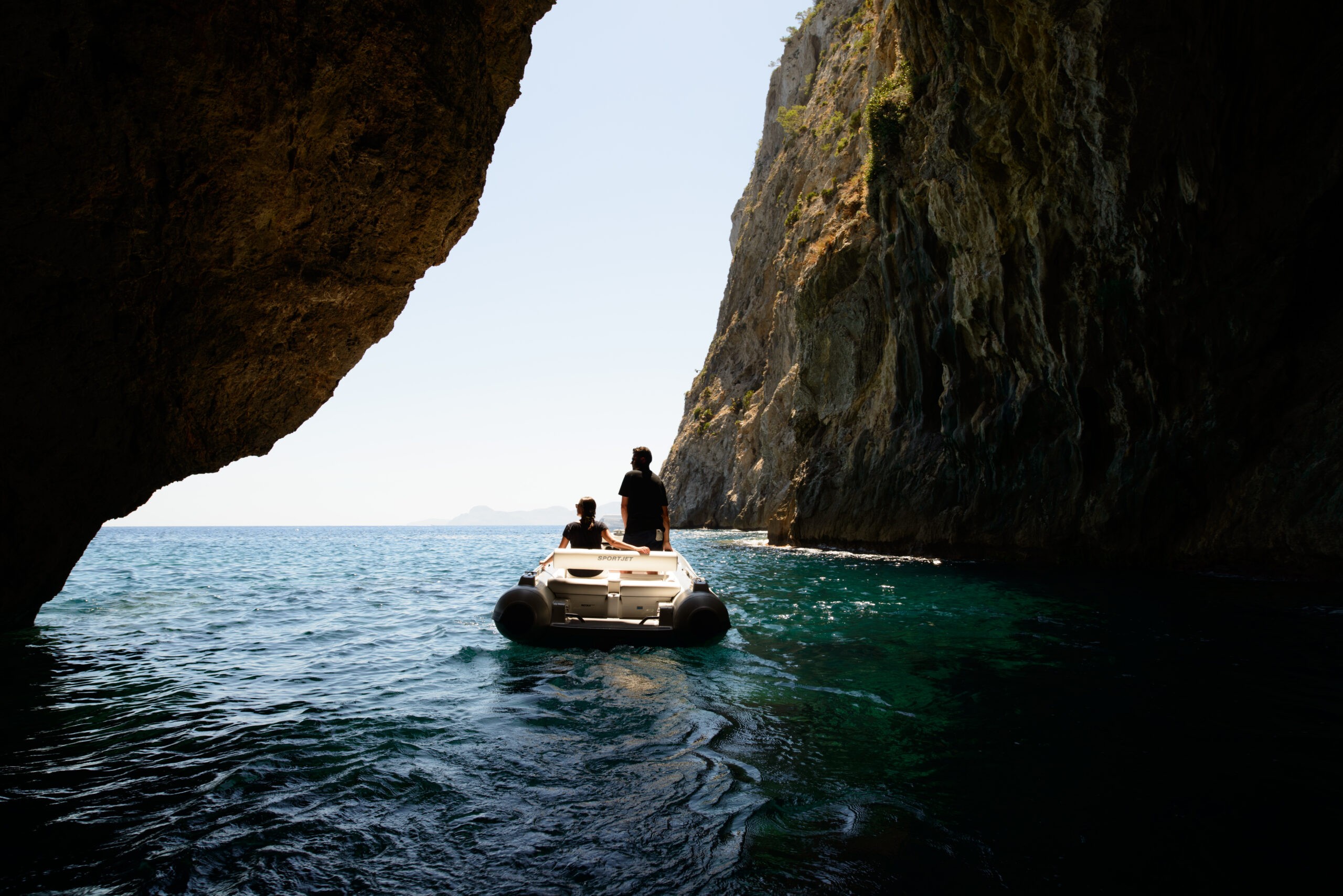 Two people on a RIB tender exploring a scenic cave leading to the open sea.