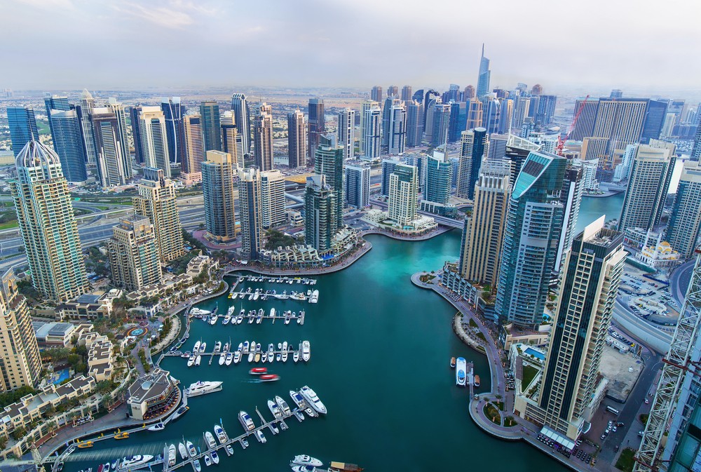 Aerial view of a modern cityscape with tall skyscrapers, a winding marina, and numerous yachts.