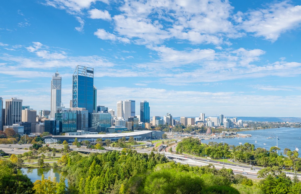 A vibrant cityscape with modern skyscrapers, lush greenery, and a river under a blue sky.