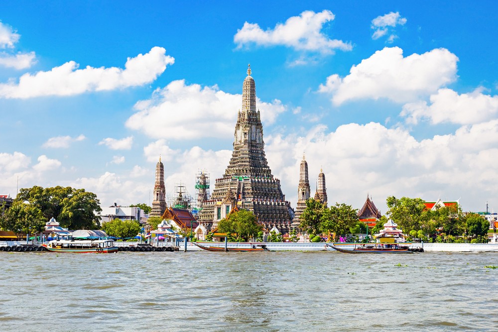 A majestic temple by the river with boats and lush greenery under a blue sky.
