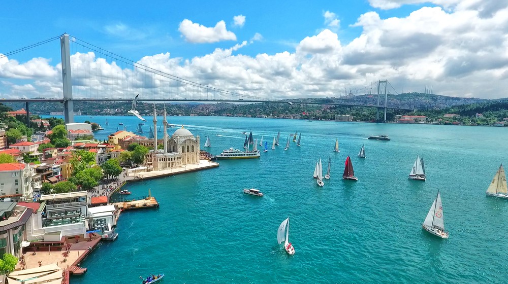 A vibrant coastal scene with boats sailing and a bridge spanning the blue water.