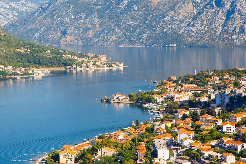Scenic coastal town with orange-roofed houses, nestled between lush mountains and calm waters.