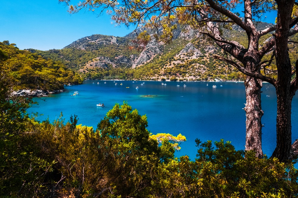 Serene blue lake surrounded by lush green hills and trees with boats floating peacefully.