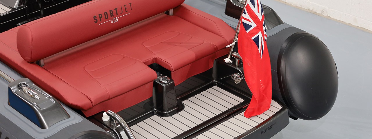 The red upholstered seat of a Williams SportJet 435 tender boat with a British flag at the rear.
