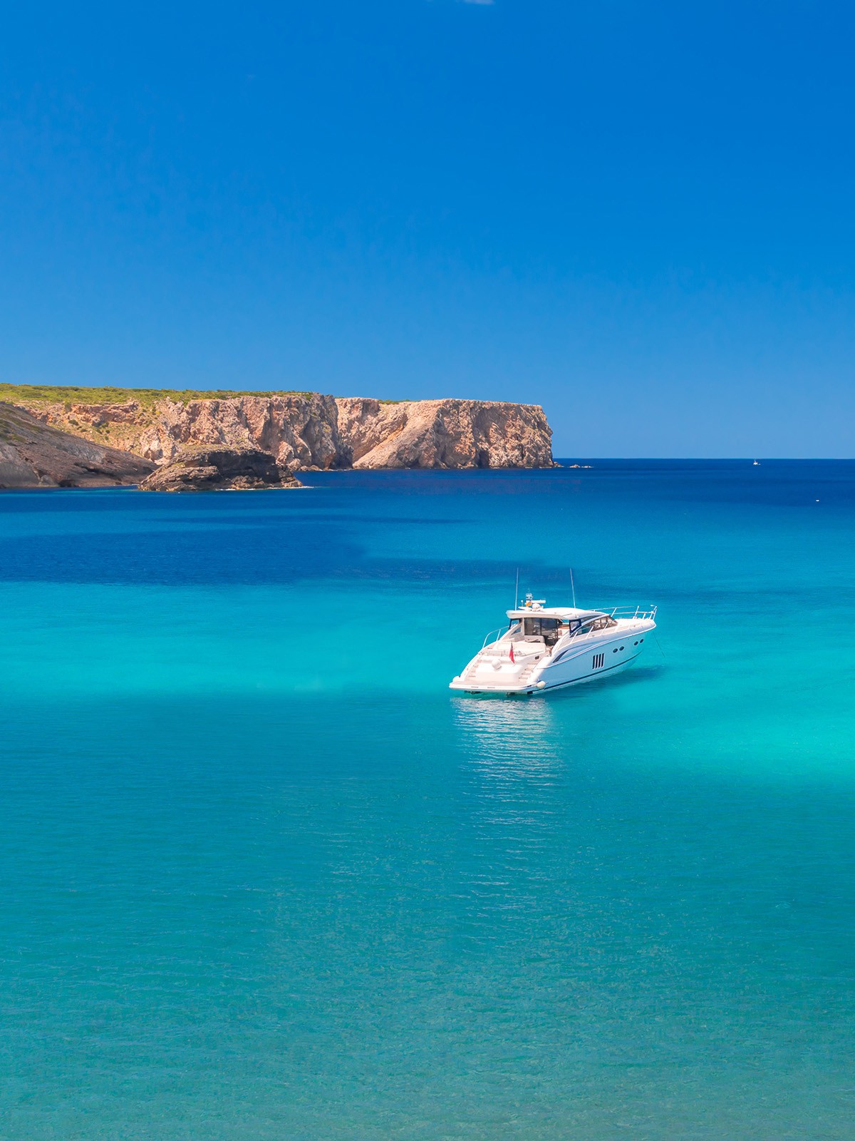 A luxury superyacht anchored in crystal-clear turquoise waters with rocky cliffs in the background