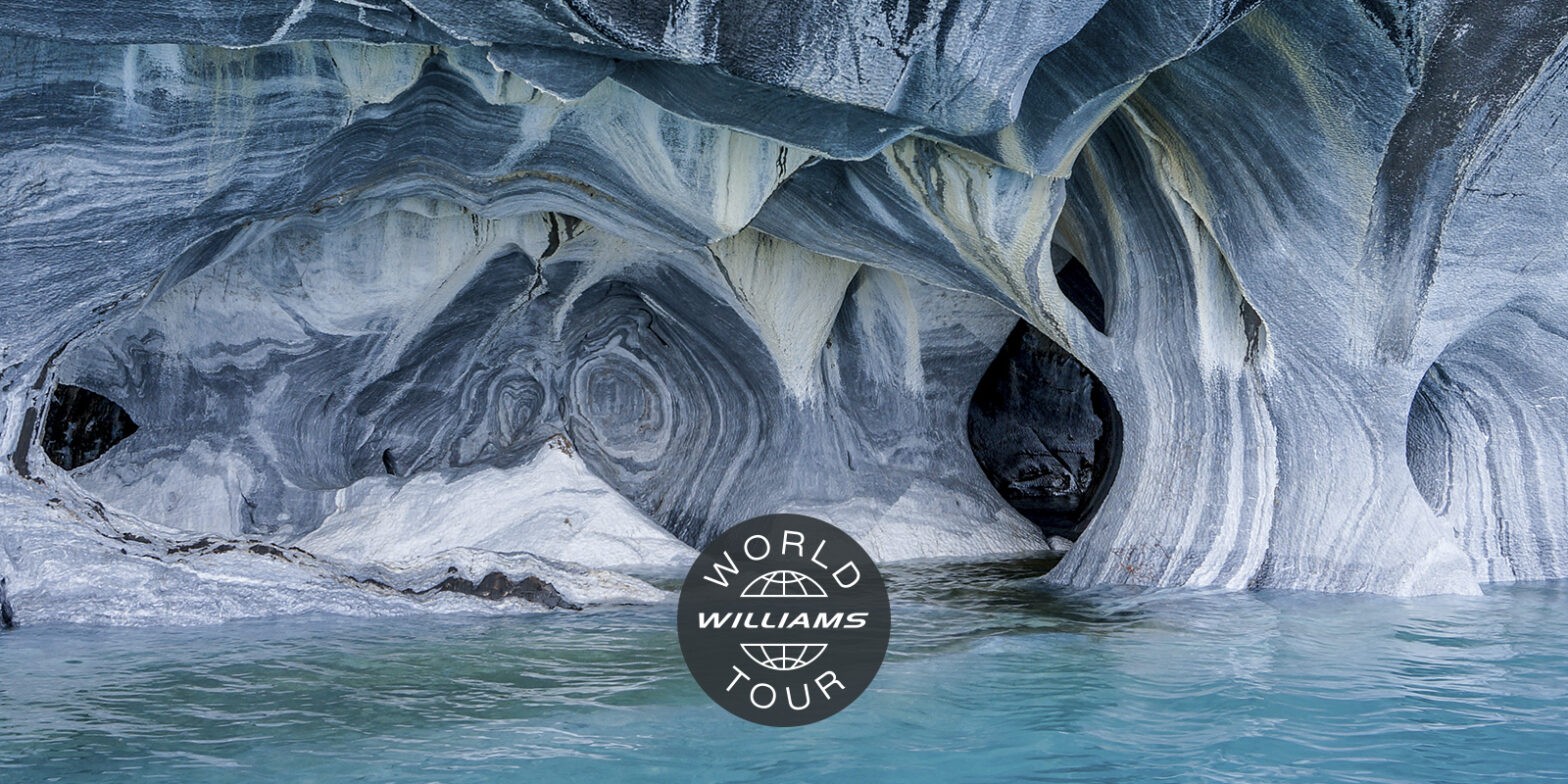 Intricate rock formations by the water with "Williams World Tour" logo in the foreground