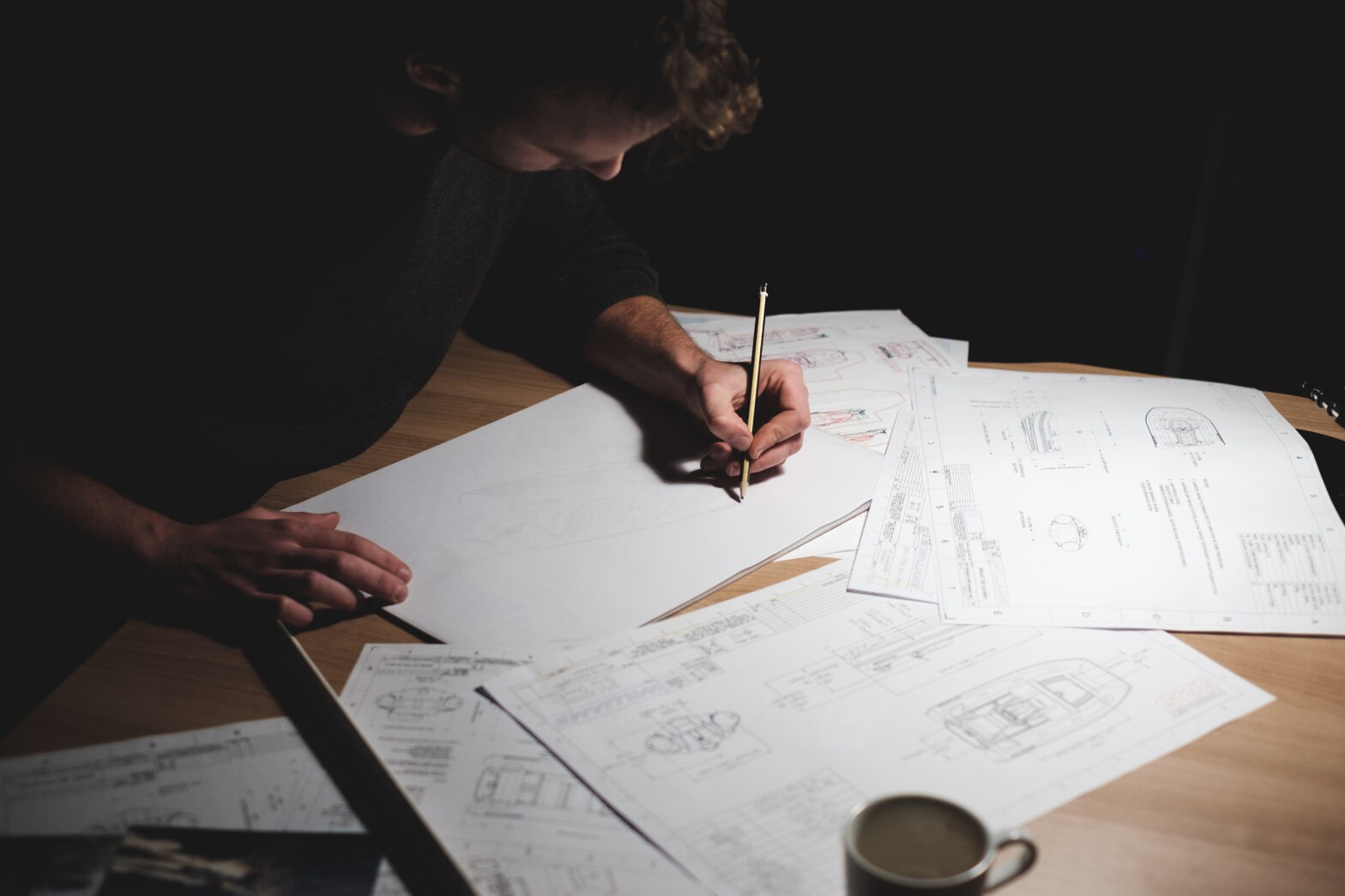 A person working on boat designs and sketches at a desk, surrounded by blueprints.