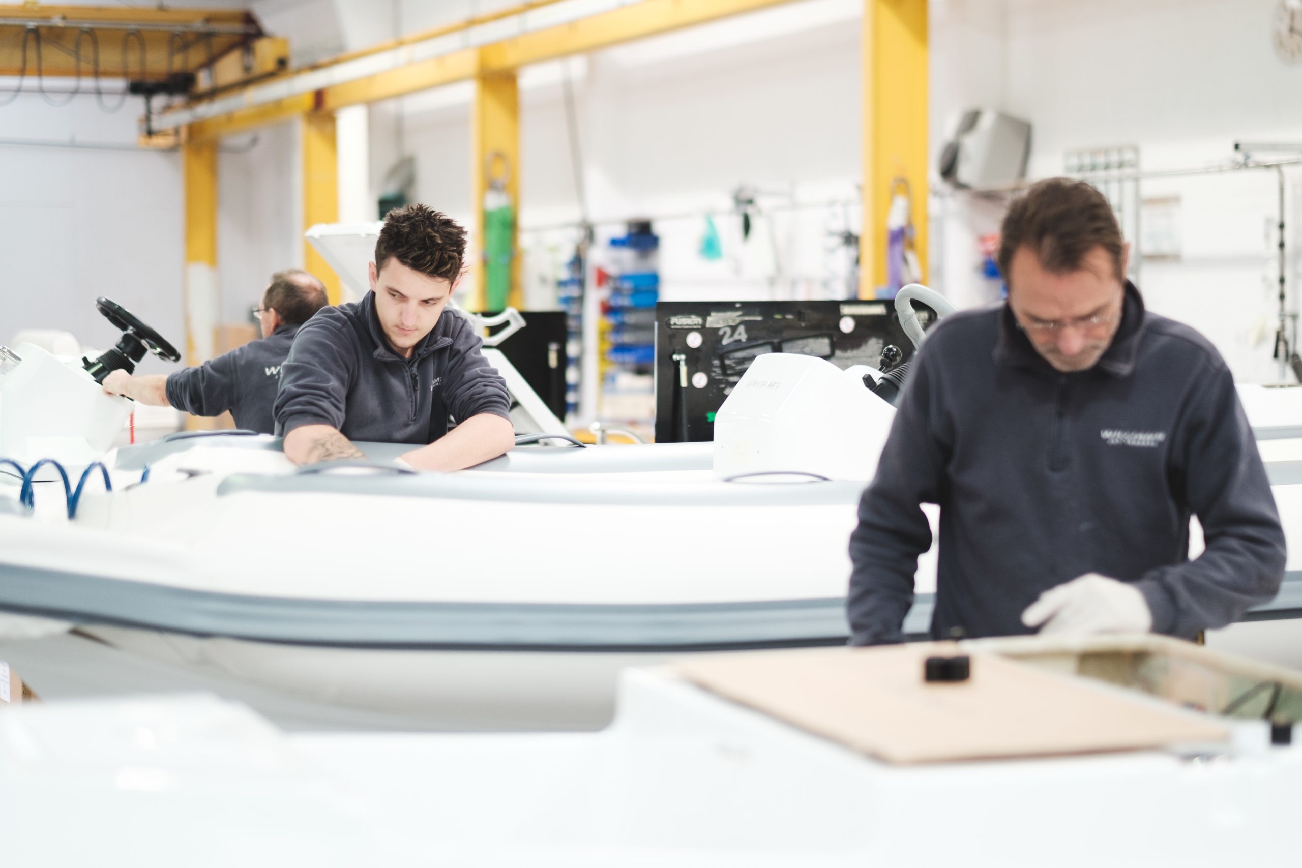 Two men working on assembling boats inside a Williams factory, focusing on details.