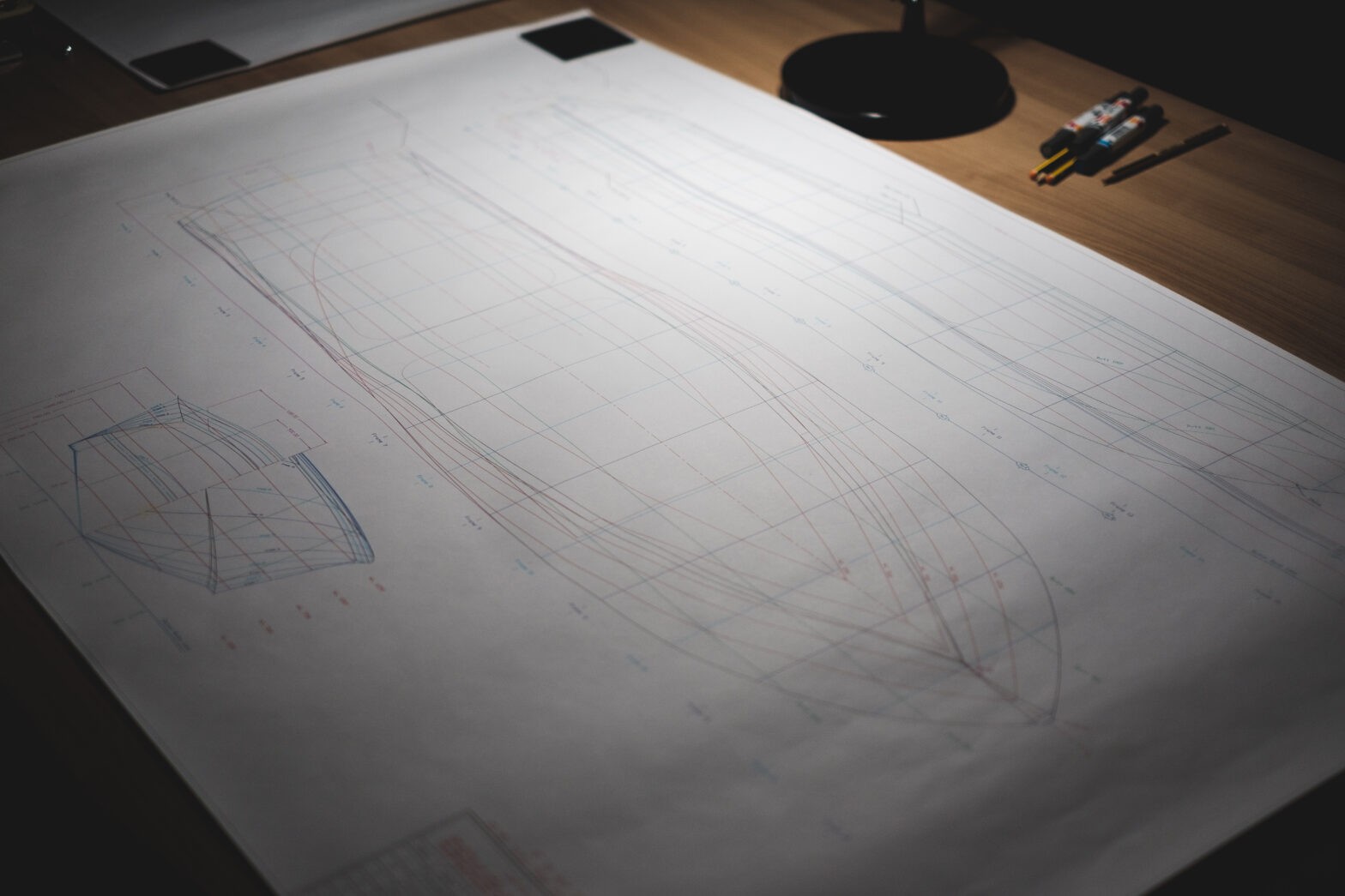 Blueprints of a boat design spread out on a table, with pens nearby.