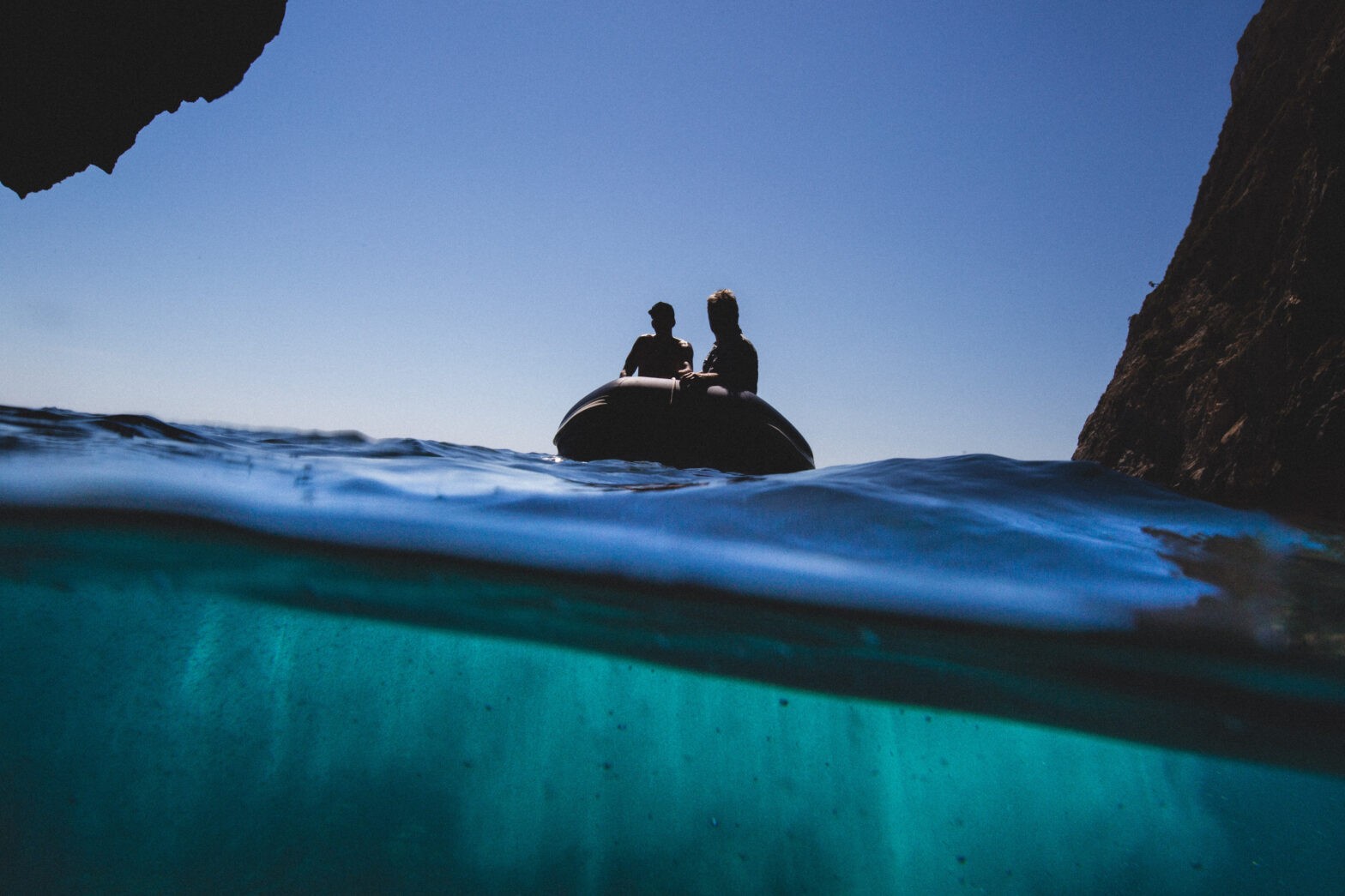 Silhouette of two people in a boat on the water with underwater view.