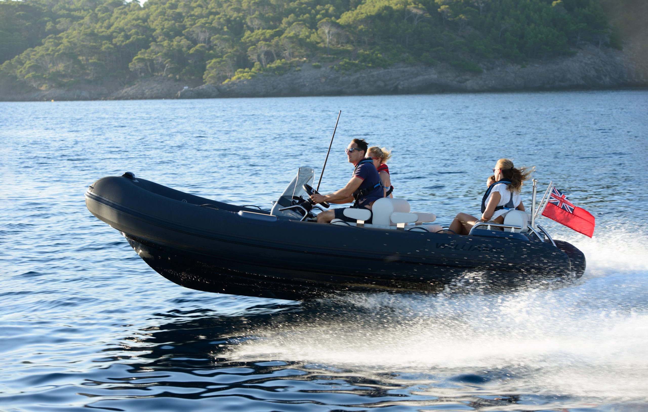 A family enjoying a fast ride on a midsized yacht tender with scenic green hills behind.