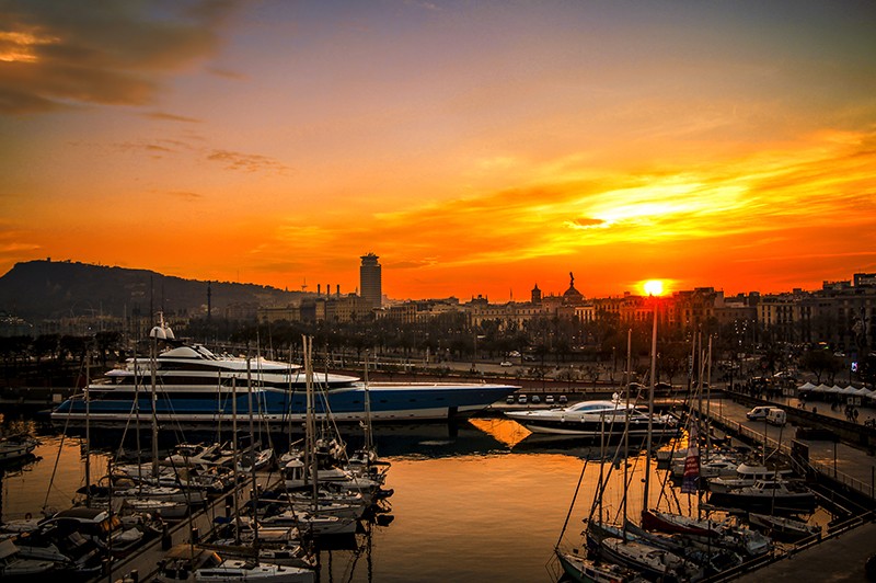 A stunning sunset over a marina filled with yachts, against a city skyline backdrop.