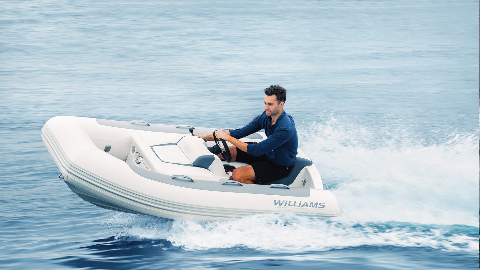 A man driving a Williams MiniJet 280 (small inflatable tender) at high speed on the water