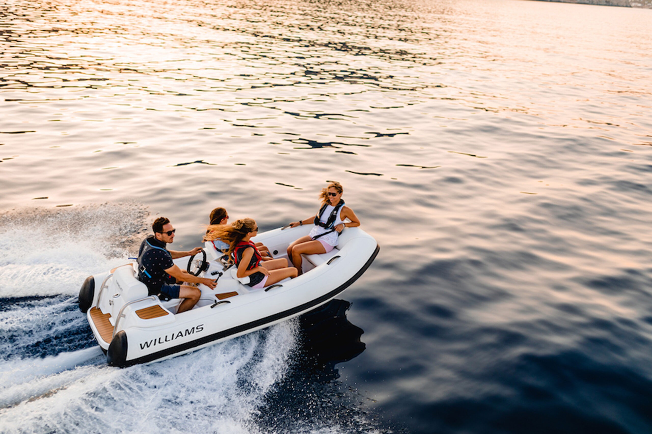 A group of people enjoying a ride on a Williams TurboJet 325, a small tender boat, during a beautiful sunset.
