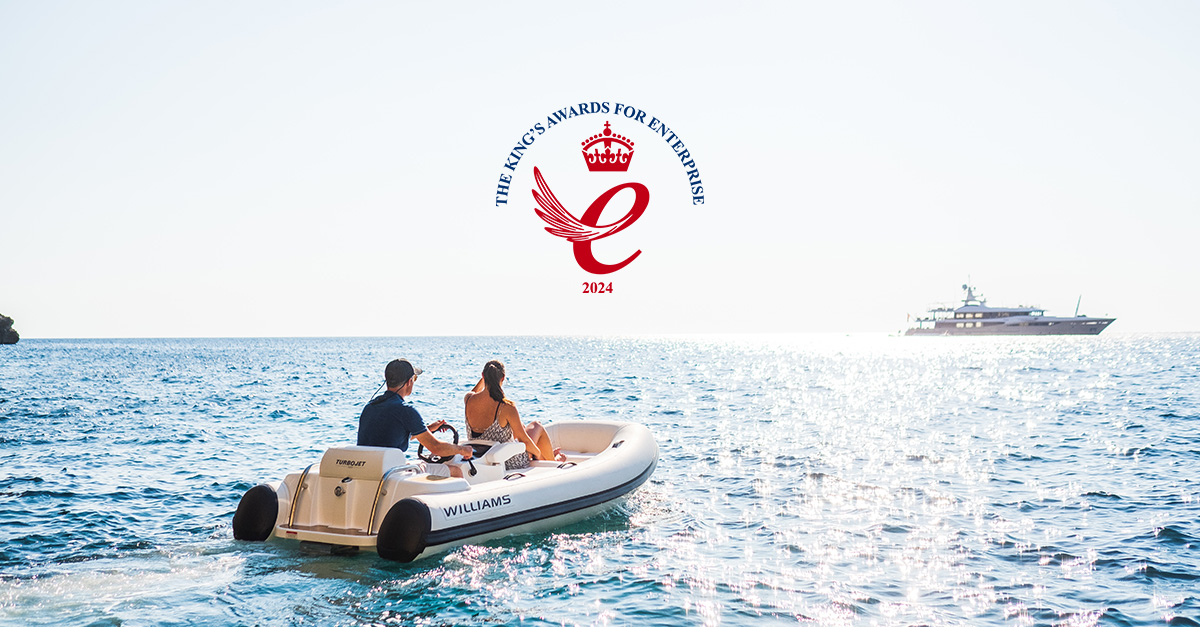 A couple on a Williams Jet Tender heading towards a luxury yacht, displaying The King's Award for Enterprise.