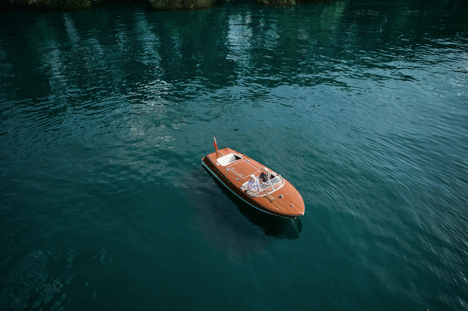 Wooden boat cruising on calm, clear water with two passengers onboard